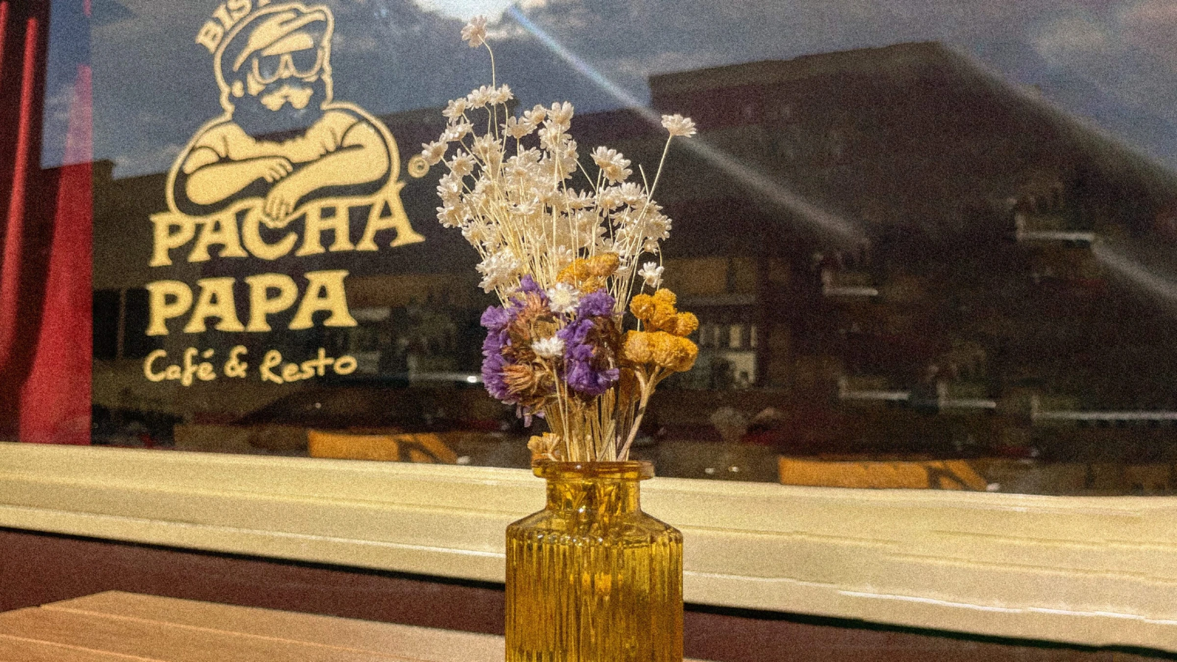 Vitrine du Bistro Pacha Papa à Lyon : logo (homme barbu à casquette) gravé sur la vitre et bouquet de fleurs séchées sur le comptoir